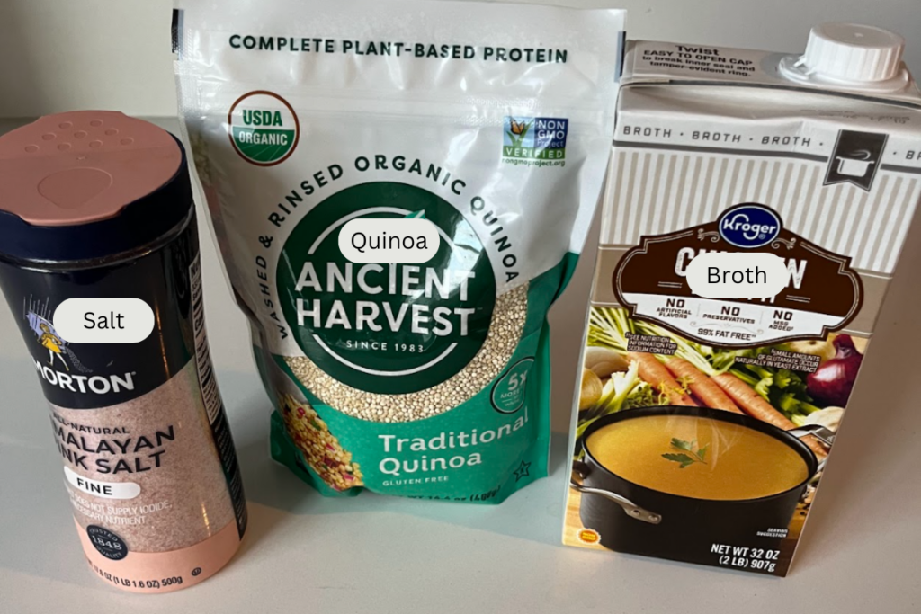 Quinoa, broth, and salt laid out on a counter.