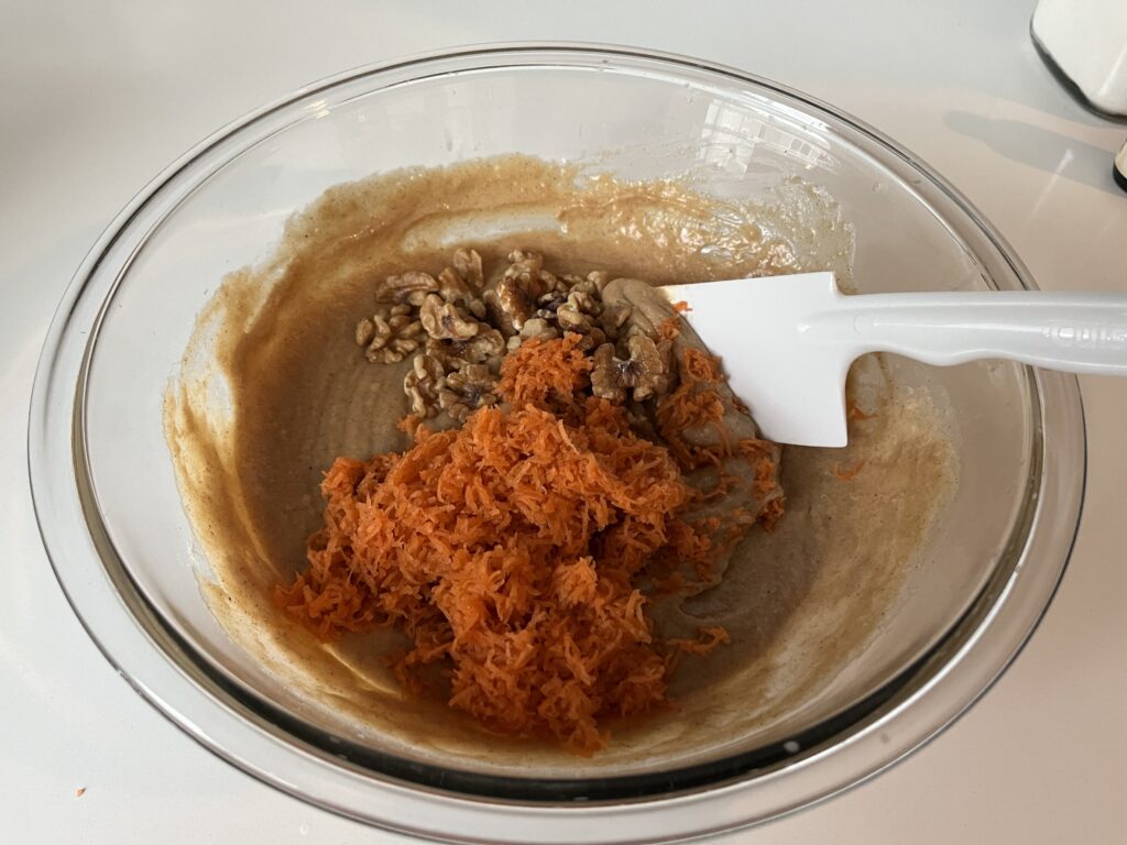 carrot cake batter with carrots and walnuts in a glass mixing bowl.