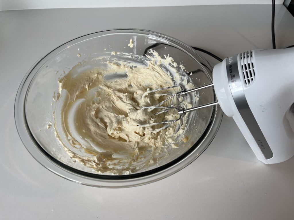 cream cheese frosting being made in a glass mixing bowl.