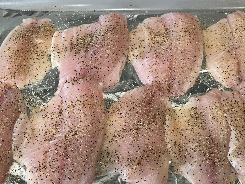 Seasoned tilapia fillets on a baking sheet.