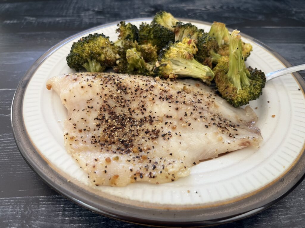 Tilapia on a plate with steamed broccoli.
