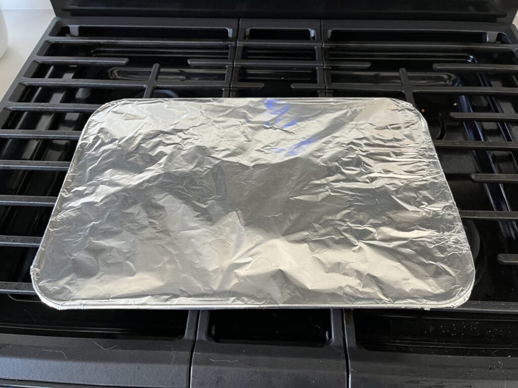 Baking dish of scalloped potatoes on a stove covered in foil.