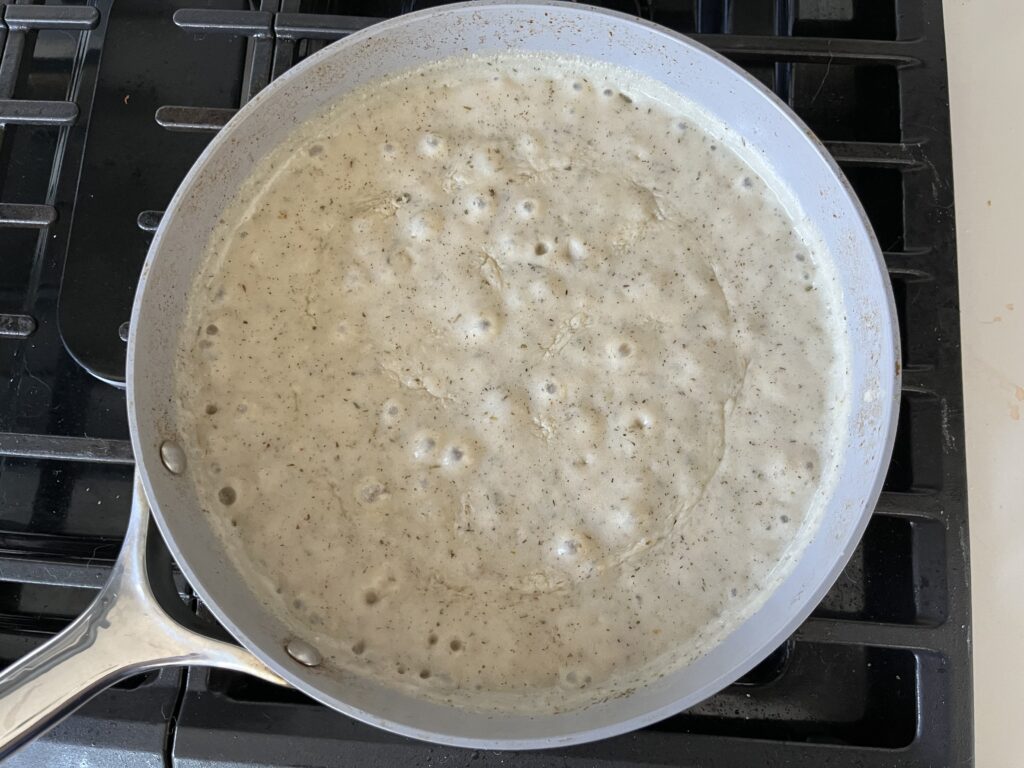 Scalloped potatoes cream sauce simmering in a pan.