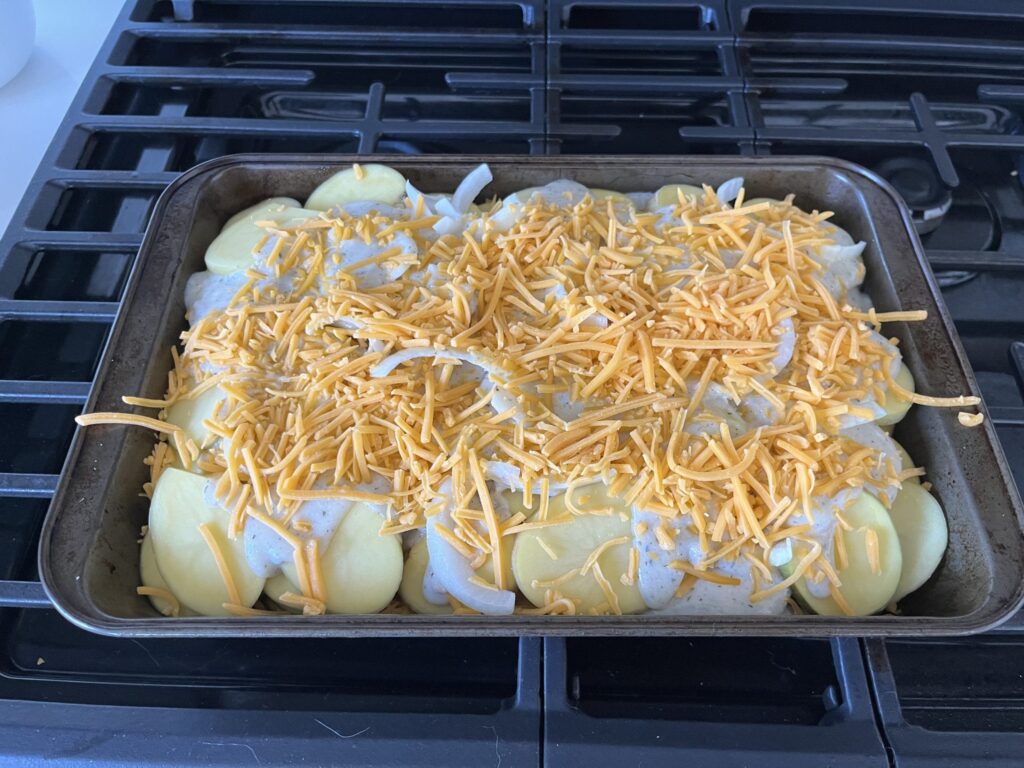 Sliced potatoes layered in a baking dish with onions, sauce, and cheese on top.