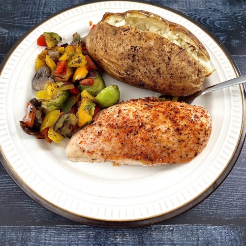 Baked chicken served on a plate with veggies and potatoes.