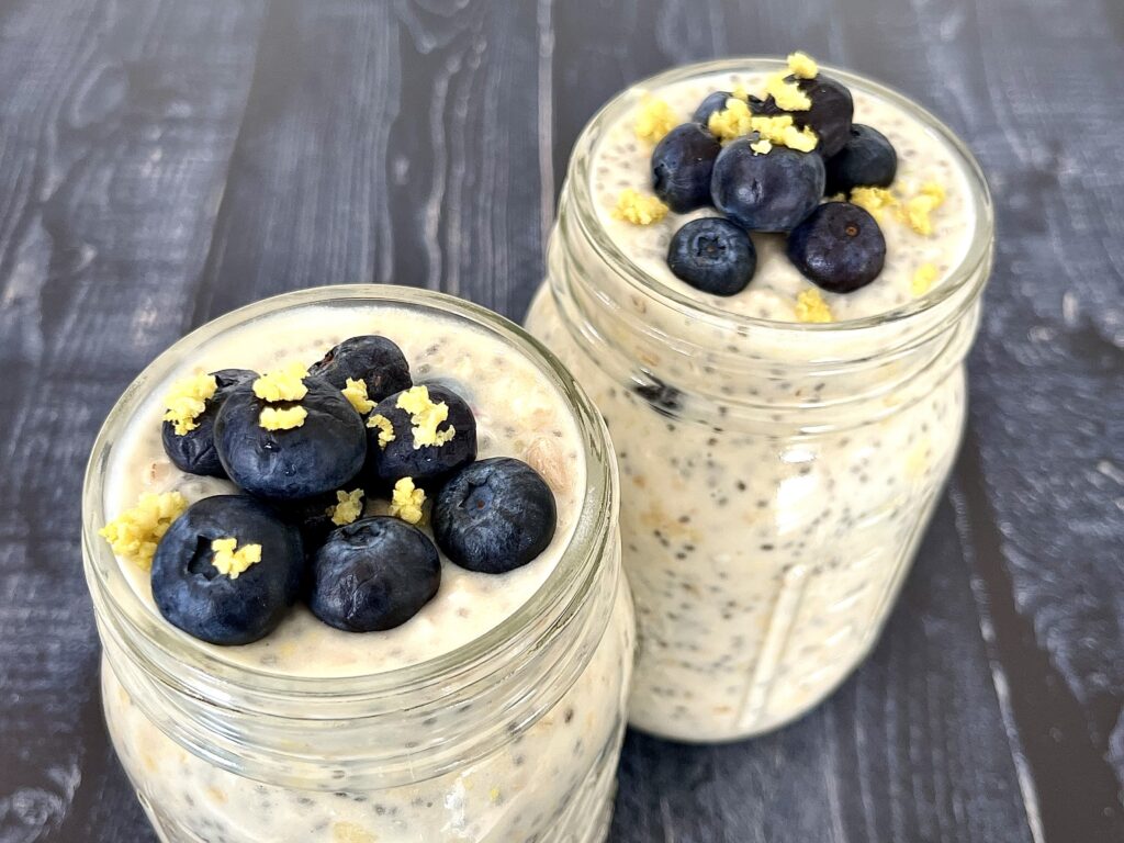 2 glass jars of overnight oats with blueberries and lemon zest on top.