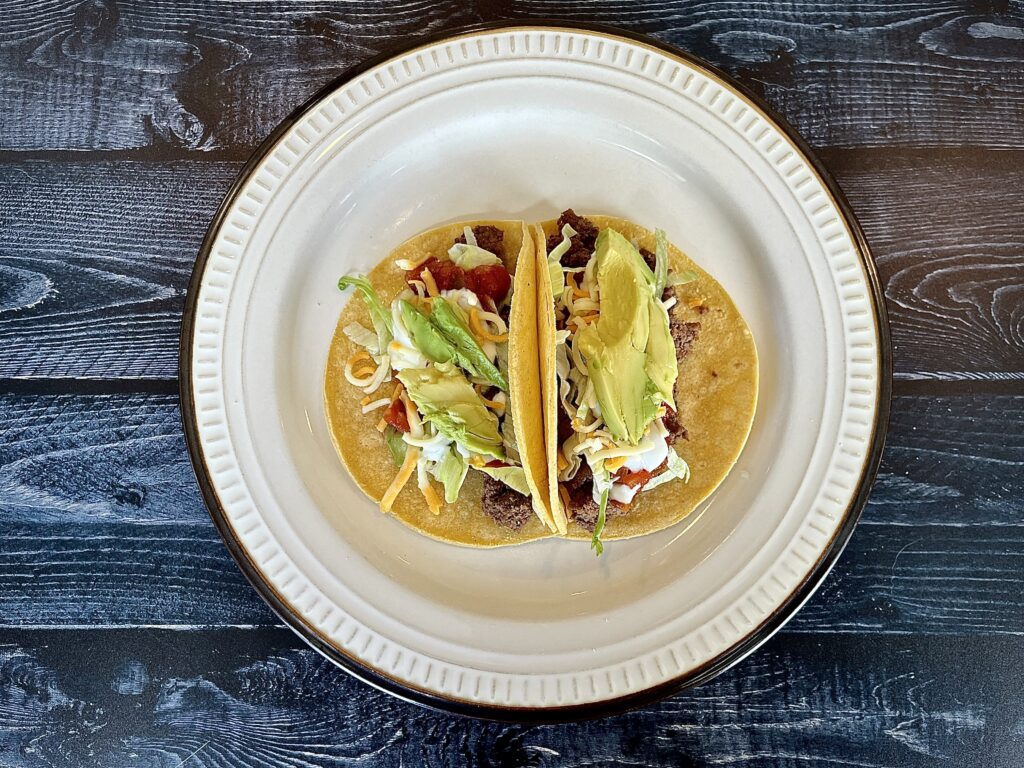 Two beef tacos on a plate with lettuce and avocado.