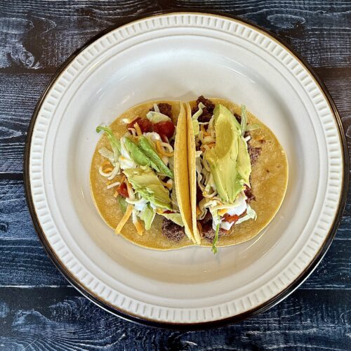 Two beef tacos on a plate with lettuce and avocado.