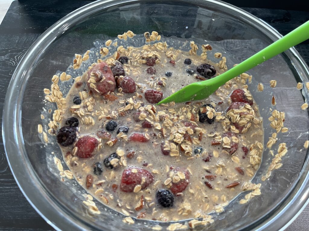A glass mixing bowl with oats and frozen berries.