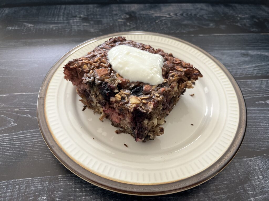 A slice of berry baked oatmeal on a plate topped with yogurt.