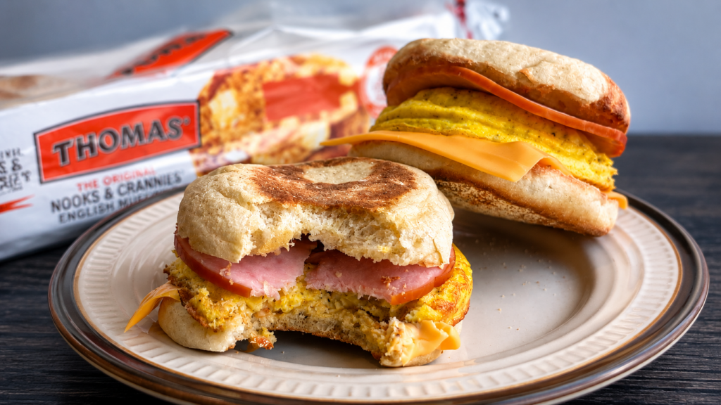 A plate with two homemade egg mcmuffins, one missing a bite. A box of English muffins in the background.