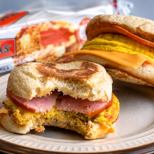 A plate with two homemade egg mcmuffins, one missing a bite. A box of English muffins in the background.