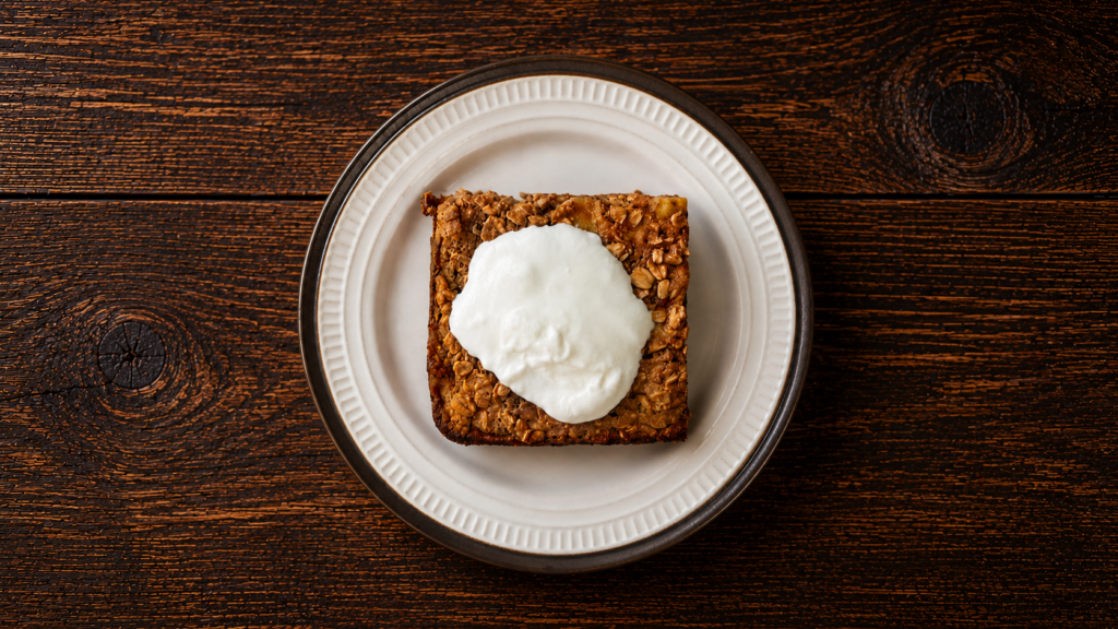 A square of baked banana oatmeal on a plate topped with yogurt.