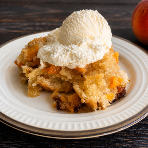 A serving of easy peach cobbler with fresh peaches on a plate topped with vanilla ice cream.