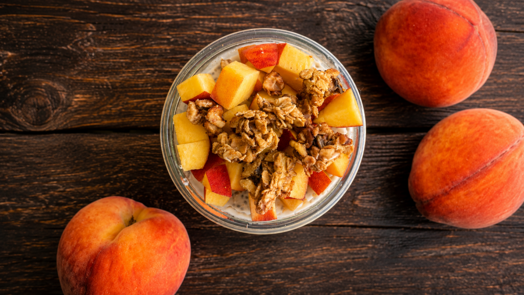 A jar of peaches and cream overnight oats topped with diced peaches and granola, three peaches surrounding it. 