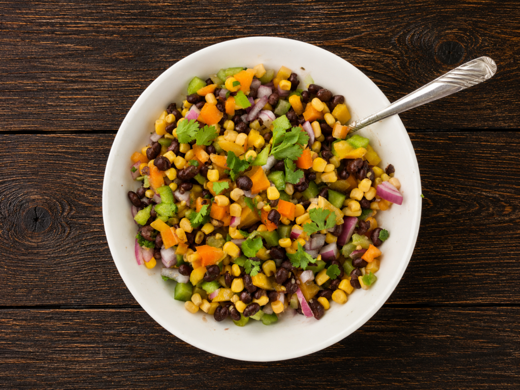 A bowl of corn and black bean salad with a spoon sticking out.