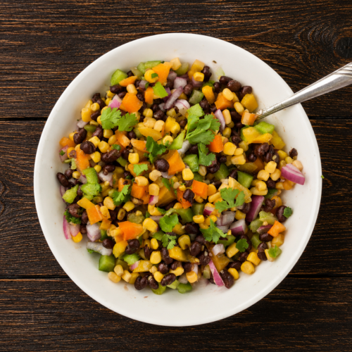 A bowl of corn and black bean salad with a spoon sticking out.
