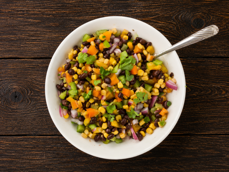 A bowl of corn and black bean salad with a spoon sticking out.