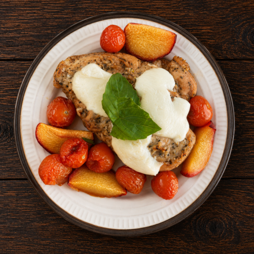 A plate of peach chicken topped with mozzarella and basil surrounded by sliced peaches and cherry tomatoes.