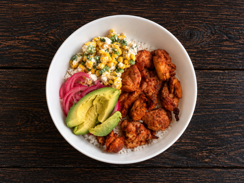A Mexican street corn chicken bowl with cilantro lime rice, marinated chicken, Mexican street corn topping, pickled onion, and avocado.