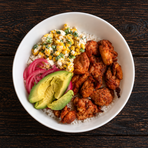 A Mexican street corn chicken bowl with cilantro lime rice, marinated chicken, Mexican street corn topping, pickled onion, and avocado.