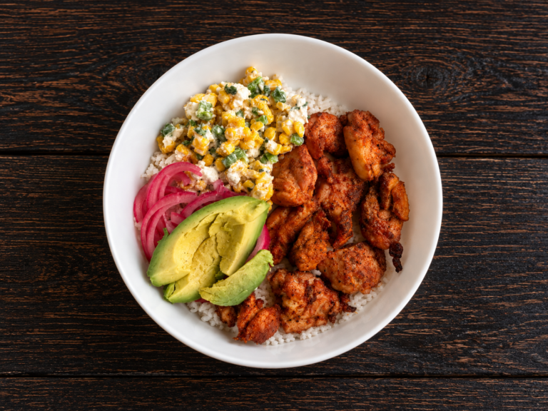 A Mexican street corn chicken bowl with cilantro lime rice, marinated chicken, Mexican street corn topping, pickled onion, and avocado.