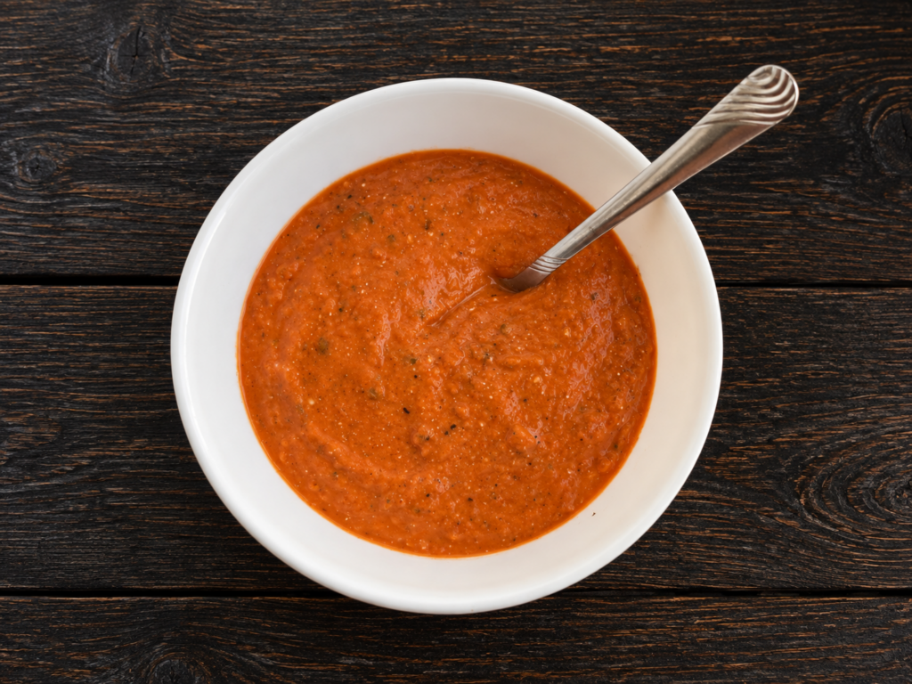 A bowl of roasted tomato soup with a spoon sticking out.