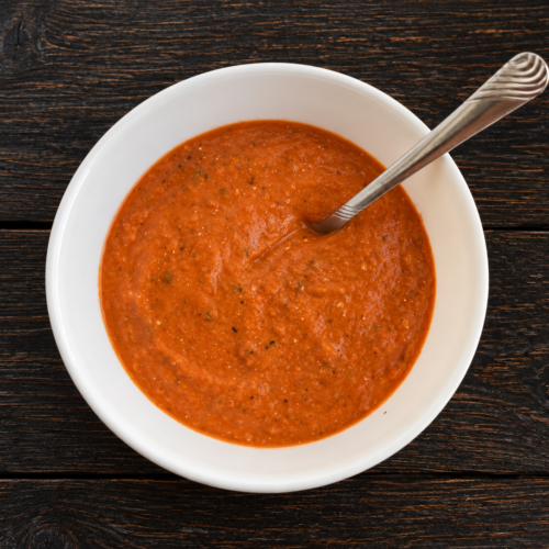 A bowl of roasted tomato soup with a spoon sticking out.